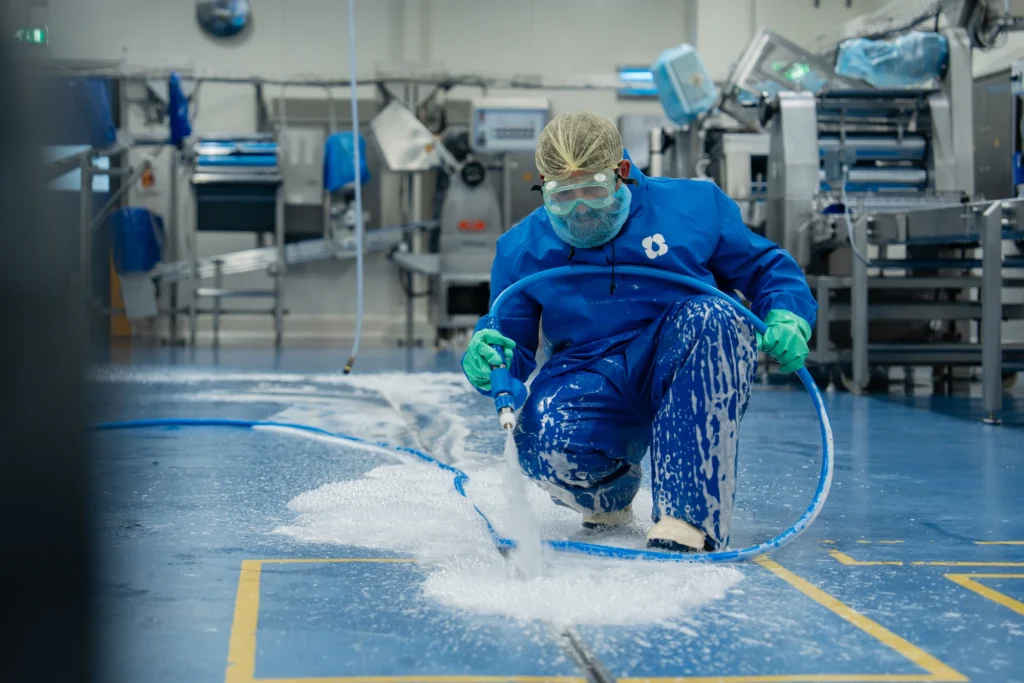 Medewerker in beschermende kleding reinigt een productievloer in de voedingsindustrie