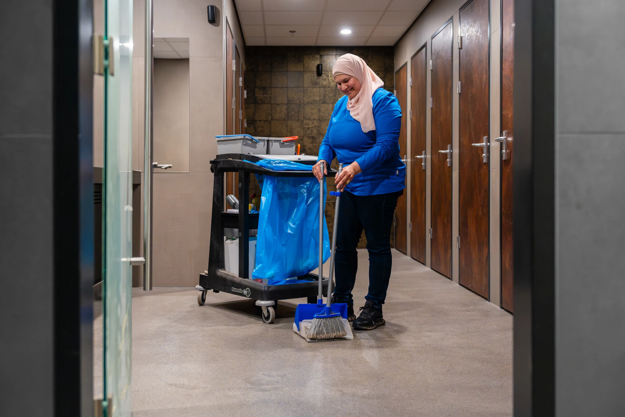 Medewerker met schoonmaakkar in een kantoorgang